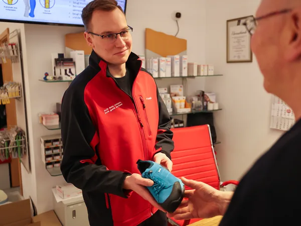 Paul Leyske gibt einem Kunden am Tresen einen Schuh in die Hand